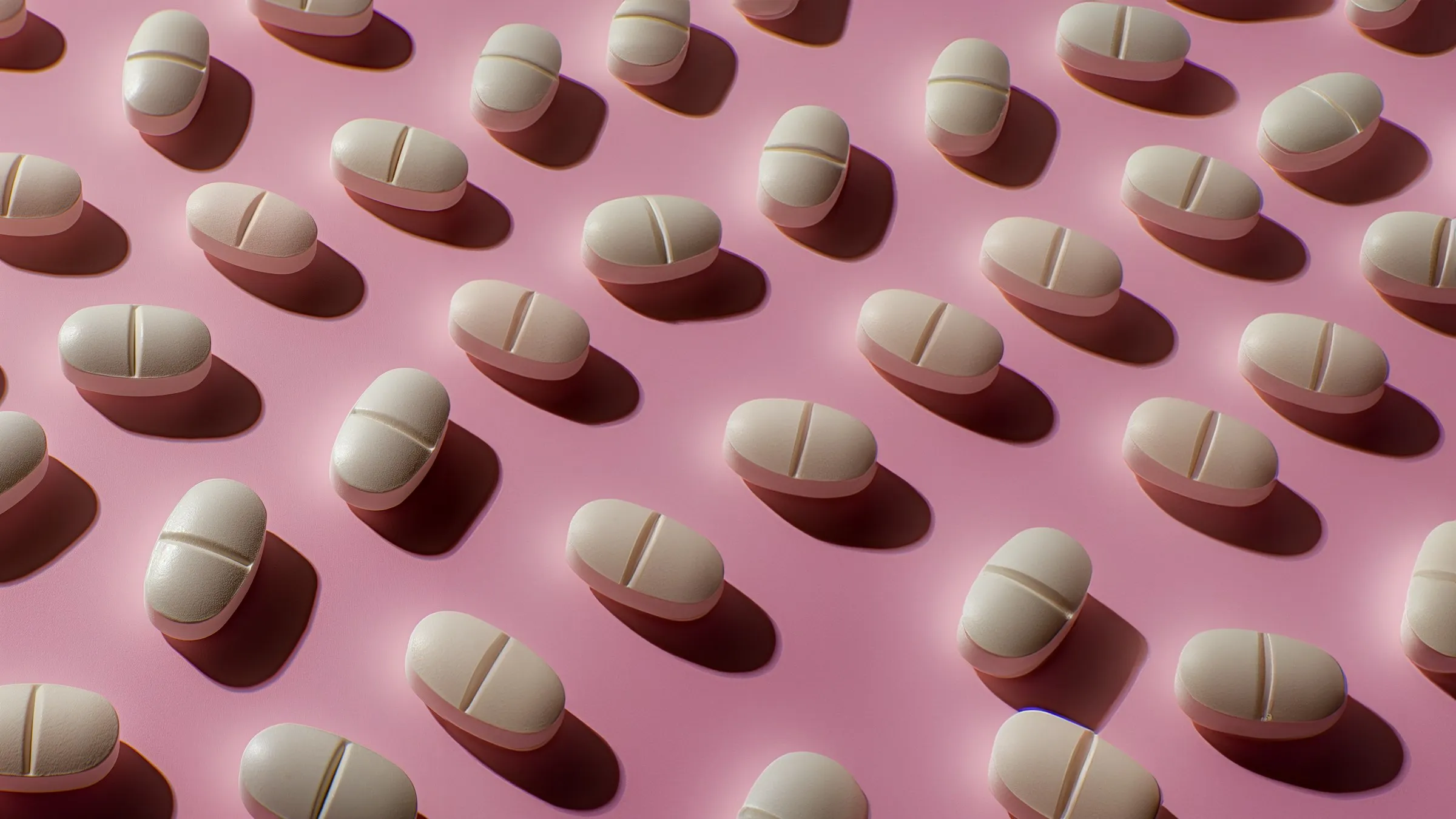 Multiple white, capsule-shaped pills arranged in a staggered pattern on a pink background.
