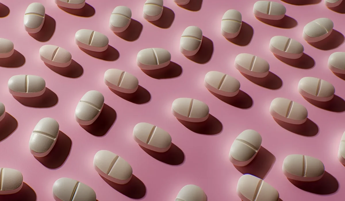 Multiple white, capsule-shaped pills arranged in a staggered pattern on a pink background.